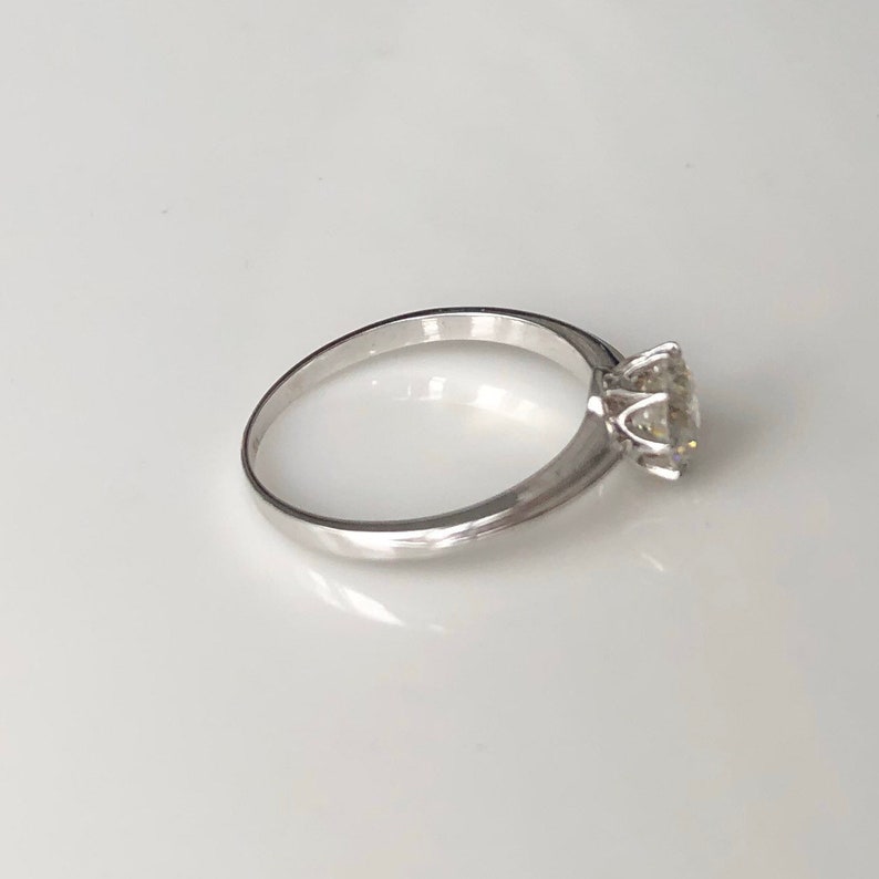May include: A simple silver band ring with a single, round, clear gemstone set in a four-prong setting.