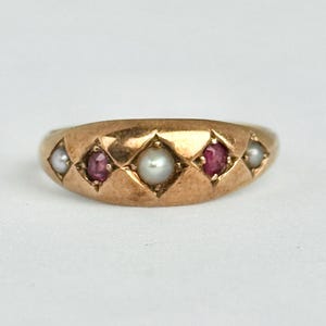 Op de afbeelding: Een gouden ring met afwisselend parels en rode edelstenen. Het ontwerp van de ring bevat ruitvormige zettingen. De ring heeft een gepolijst oppervlak. De edelstenen zijn in een herhalend patroon geplaatst.
