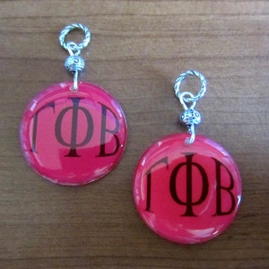 May include: Two red circle charms with silver chains and beads. The charms have black lettering that reads "ΓΦΒ".