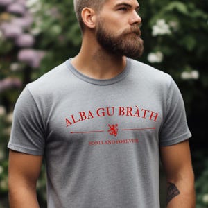Puede incluir: Una camiseta gris con un estampado rojo que dice "Alba gu Bràth" y "Scotland Forever".
