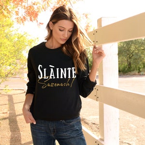 May include: A black long-sleeved sweatshirt with the text "Sl&aacute;inte Sas&oacute;nach!" in white and gold lettering.
