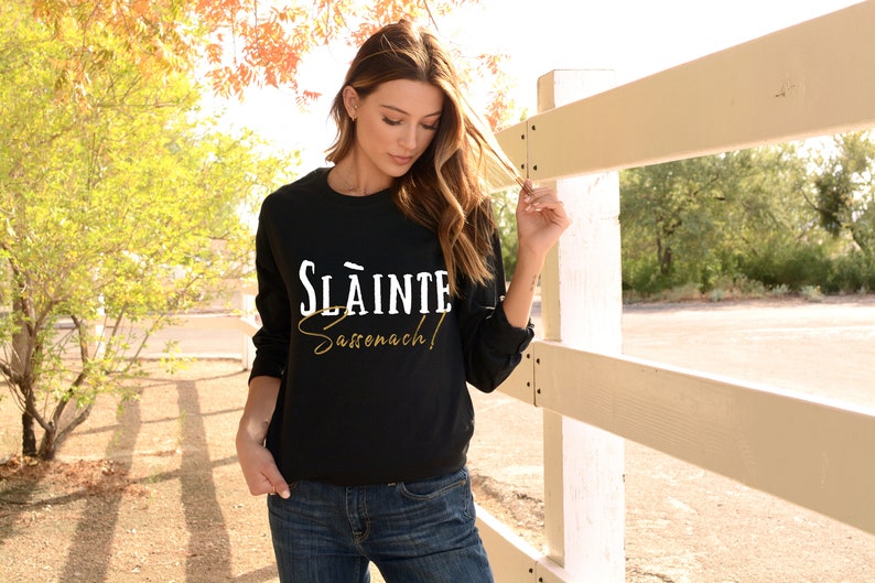 May include: A black long-sleeved sweatshirt with the text "Sl&aacute;inte Sas&oacute;nach!" in white and gold lettering.