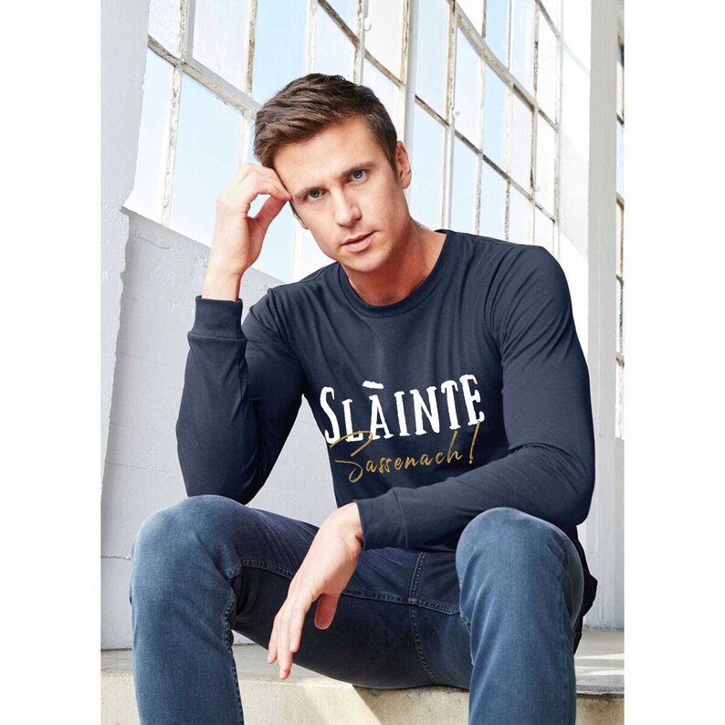 May include: A navy blue long-sleeve shirt with white text that reads "Slainte Sassenach!" in a vintage style font.
