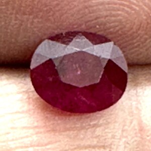 May include: A deep red gemstone with a faceted cut. The gemstone is round and has a high polish.