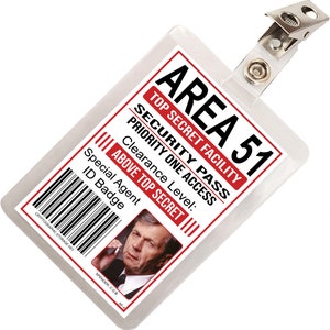 May include: A white plastic ID badge with a red border and the text "AREA 51" in red. The badge also has the text "TOP SECRET FACILITY", "SECURITY PASS", "PRIORITY ONE ACCESS", "Clearance Level: ABOVE TOP SECRET", "Special Agent ID Badge" in red. A photo of a man is in the bottom right corner of the badge.