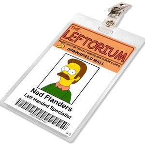 May include: A white plastic ID badge with a yellow and orange header that reads "THE LEFTORIUM EVERYTHING FOR THE LEFT HANDED MAN WOMAN & CHILD SPRINGFIELD MALL". The badge has a photo of a cartoon character with yellow skin, brown hair, and a mustache. The text "Ned Flanders Left Handed Specialist" is printed below the photo. A barcode with the number "00056190624561" is printed below the text. The badge has a small metal clip at the top.