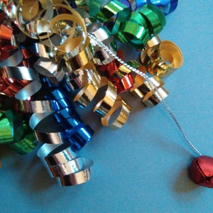 Pode incluir: Um monte de fita de curling colorida com um sino vermelho preso a um cordão prateado.