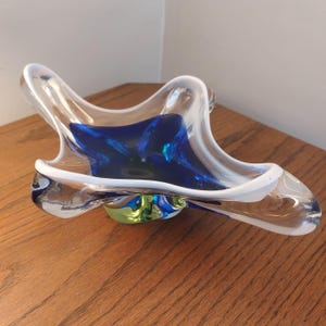 May include: A star-shaped glass bowl featuring a deep blue centre encased in clear glass with a thick white rim. The bowl has an irregular, organic form with four distinct points extending outward, creating a sculptural appearance with smooth curves.