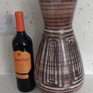 May include: A brown and white ceramic vase with a geometric pattern. The vase is sitting on a white countertop with a bottle of Campo Viejo Rioja Reserva wine next to it.