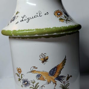 May include: White ceramic jar with a green lid and a green rim. The jar features a floral design with a bird and the word "Ligueil" written on the lid.