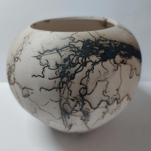 May include: A spherical, off-white ceramic bowl with a wide opening. The bowl is decorated with black, organic, lightning-like patterns. The interior is a lighter shade of beige. The bowl is a decorative piece for the home.
