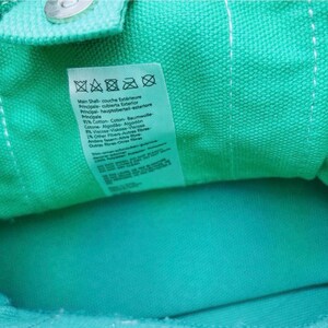 May include: Close-up of a teal fabric with a white label. The label has text in multiple languages, including English, French, and German, detailing the fabric's composition: 91% cotton, 8% viscose, and 1% other fibres.
