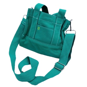May include: Teal canvas tote bag with a detachable shoulder strap and top handles. The bag features a front pocket with three green stripes and white stitching details. The adjustable strap is made of the same teal canvas material.
