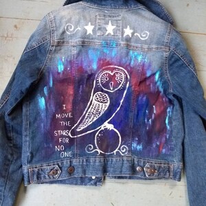 May include: A blue denim jacket with a white owl and stars painted on the back. The text "I move the stars for no one" is also painted on the back.