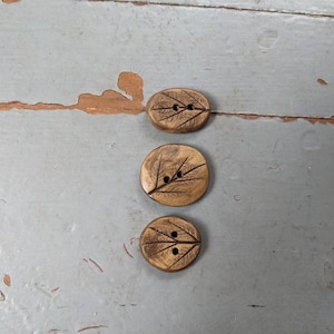 May include: Three wooden buttons with a leaf design. The buttons are brown and have a natural wood finish.