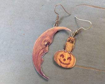 May include: A pair of Halloween-themed earrings. One earring features a crescent moon with a face, the other an owl perched on a carved pumpkin. The earrings have silver-colored hooks.