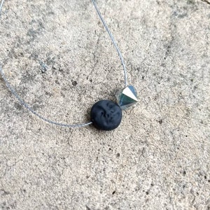 May include: A silver and black necklace with a small, faceted silver bead and a black round bead.
