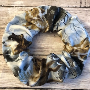 May include: A fabric hair scrunchie featuring a repeating pattern of wolves in shades of brown, black, and white against a light blue background. The accessory has a gathered, elasticized design with visible folds and a soft, textured appearance.