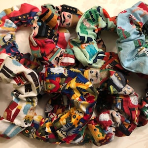 May include: A set of nine colorful fabric scrunchies featuring a repeating pattern of nutcracker soldiers. The scrunchies are made of soft, stretchy fabric and are perfect for holding back hair.