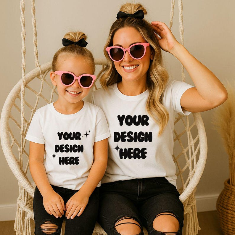 K&ouml;nnte beinhalten: Zwei Personen tragen passende wei&szlig;e T-Shirts mit dem Text "YOUR DESIGN HERE" in Schwarz. Beide tragen rosa Sonnenbrillen und haben ihre Haare hochgesteckt. Sie sitzen in einem Korbstuhl.