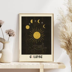 May include: A black and gold print featuring a sun, moon phases, and stars on a dark background. The print has the word "ECLIPSE" at the bottom.