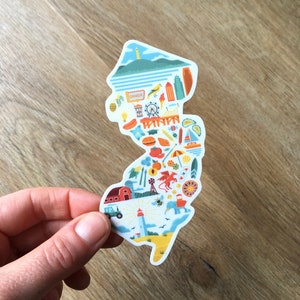 May include: A white sticker shaped like the state of New Jersey with colorful illustrations of various landmarks, food, and activities. The sticker includes a lighthouse, a farm, a Ferris wheel, a diner, a beach, and a dragon.