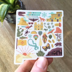 May include: A white sticker with a yellow outline in the shape of the state of New Mexico. The sticker is filled with various colorful illustrations of things associated with New Mexico, including a hot air balloon, a chile pepper, a scorpion, a dinosaur, a church, a mountain, a butterfly, a bear, and a sunset. The text '@fleurdesign.co' is at the bottom of the sticker.