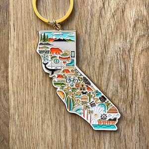 Peut inclure: Porte-cl&eacute;s en m&eacute;tal dor&eacute; en forme de l'&eacute;tat de Californie, avec un contour d&eacute;taill&eacute; de l'&eacute;tat et diverses ic&ocirc;nes repr&eacute;sentant la culture californienne, notamment un palmier, une planche de surf, une plage, un phare, un s&eacute;quoia, un ours, une montagne, un taco, un v&eacute;lo, un camping-car, une baleine, un coucher de soleil, une grande roue et le texte "TRINEN".