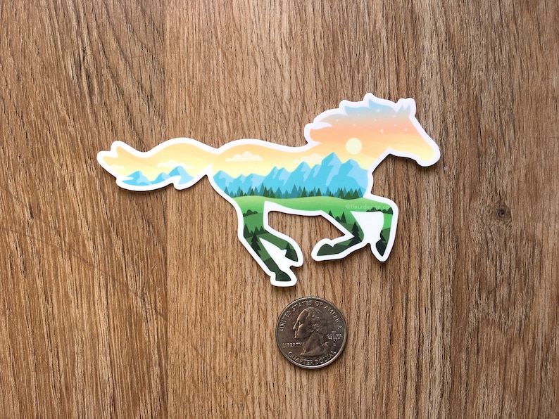 May include: A sticker depicting a running horse, with a landscape design inside. The landscape shows mountains, trees, and a sunset in yellow, orange, and blue tones. A coin is placed beside the sticker for scale.