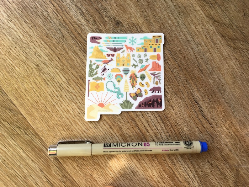 Op de afbeelding: Een sticker met een kleurrijke omtrek van de staat New Mexico met verschillende pictogrammen die de cultuur en het landschap van de staat vertegenwoordigen. De pictogrammen omvatten een luchtballon, een chilipeper, een schorpioen, een berg, een zonsondergang en een beer.