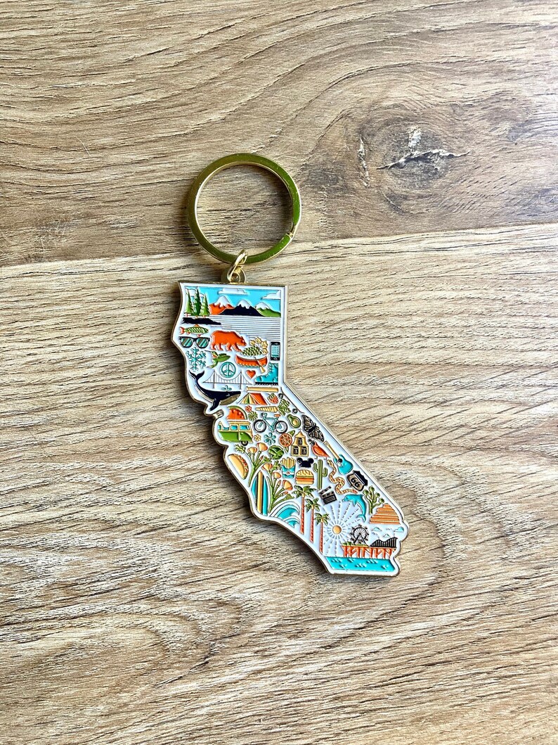 Peut inclure: Un porte-cl&eacute;s en m&eacute;tal dor&eacute; en forme de l'&eacute;tat de Californie. Le porte-cl&eacute;s est d&eacute;cor&eacute; d'illustrations color&eacute;es de divers monuments, activit&eacute;s et symboles californiens, notamment un ours, un palmier, une planche de surf, un phare et un coucher de soleil.