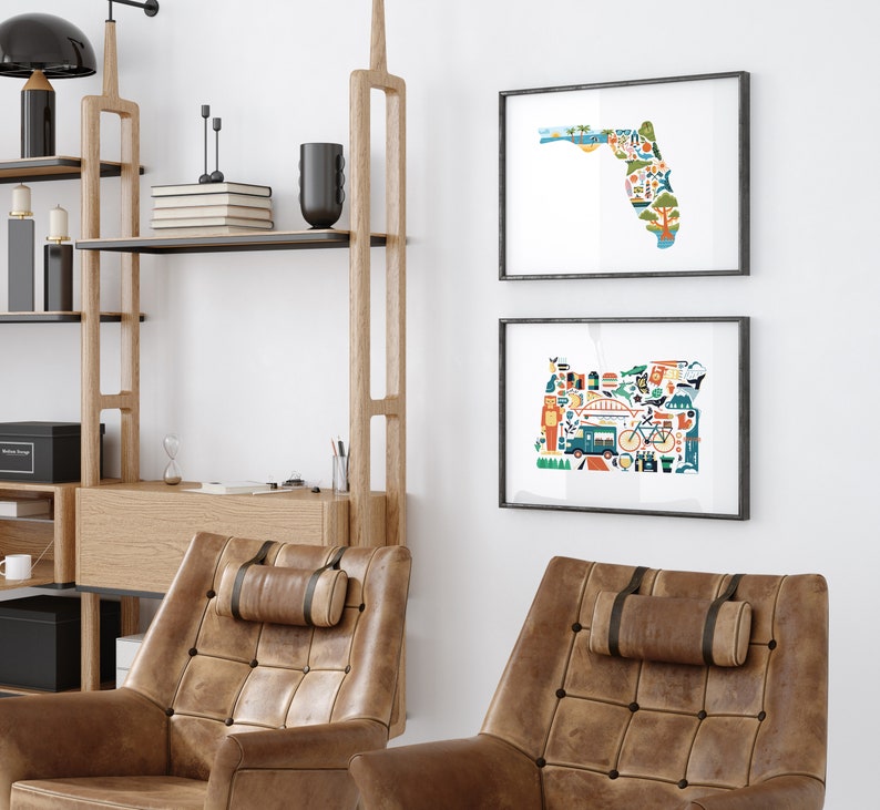 Two framed state map art prints hang on a wall. The art consists of a collection illustrated icons that form the shape of the state of Florida and Oregon. Each illustration represents that culture, natural beauty and history of the states.