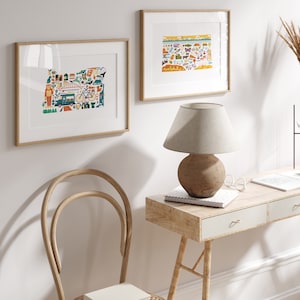 Two framed state map art prints hang on a wall. The art consists of a collection illustrated icons that form the shape of the state of Colorado and Oregon. Each illustration represents that culture, natural beauty and history of the states.