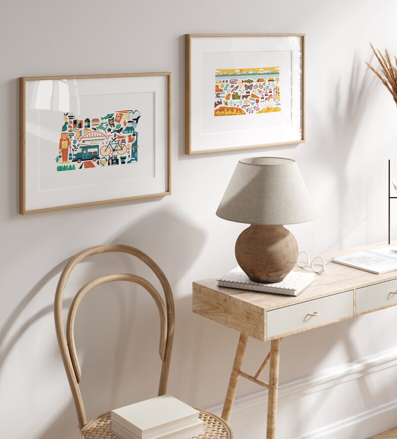 Two framed state map art prints hang on a wall. The art consists of a collection illustrated icons that form the shape of the state of Colorado and Oregon. Each illustration represents that culture, natural beauty and history of the states.