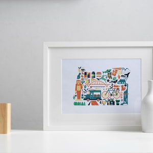 A framed Oregon map art print is leaning against a wall. The art consists of a collection illustrated icons that form the shape of the state of Oregon. Each illustration represents that culture, natural beauty and history of the state of Oregon.