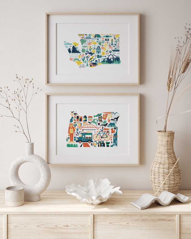 Two framed state map art prints hang on a wall. The art consists of a collection illustrated icons that form the shape of the state of Washington and Oregon. Each illustration represents that culture, natural beauty and history of the states.