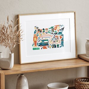 A framed Oregon map art print is leaning against a wall. The art consists of a collection illustrated icons that form the shape of the state of Oregon. Each illustration represents that culture, natural beauty and history of the state of Oregon.