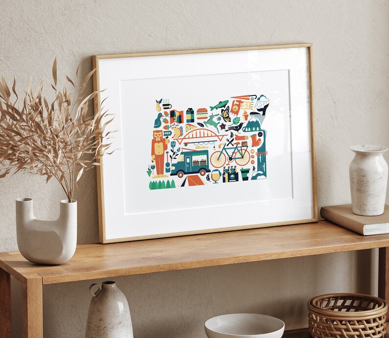 A framed Oregon map art print is leaning against a wall. The art consists of a collection illustrated icons that form the shape of the state of Oregon. Each illustration represents that culture, natural beauty and history of the state of Oregon.