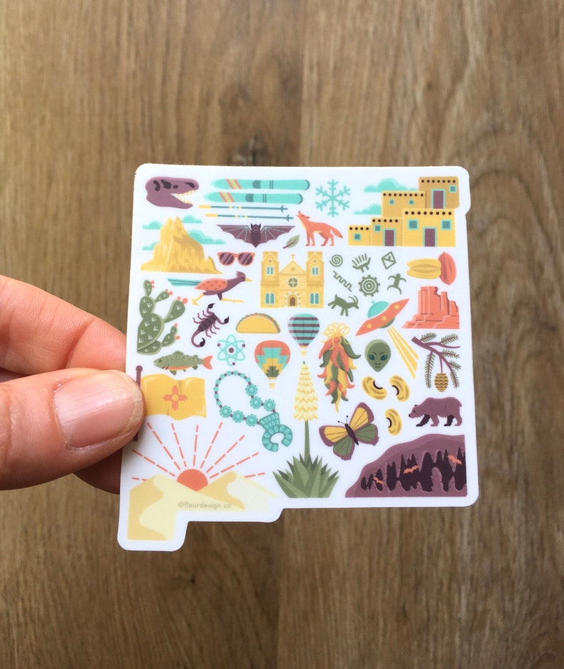 Op de afbeelding: Een witte sticker met een kleurrijke omtrek van de staat New Mexico. De sticker is gevuld met verschillende pictogrammen die de staat vertegenwoordigen, waaronder een luchtballon, een chilipeper, een schorpioen, een dinosaurus, een UFO, een beer, een kerk, een berg, een zonsondergang en een cactus. De sticker bevat ook de tekst "@laurndesigns.co".