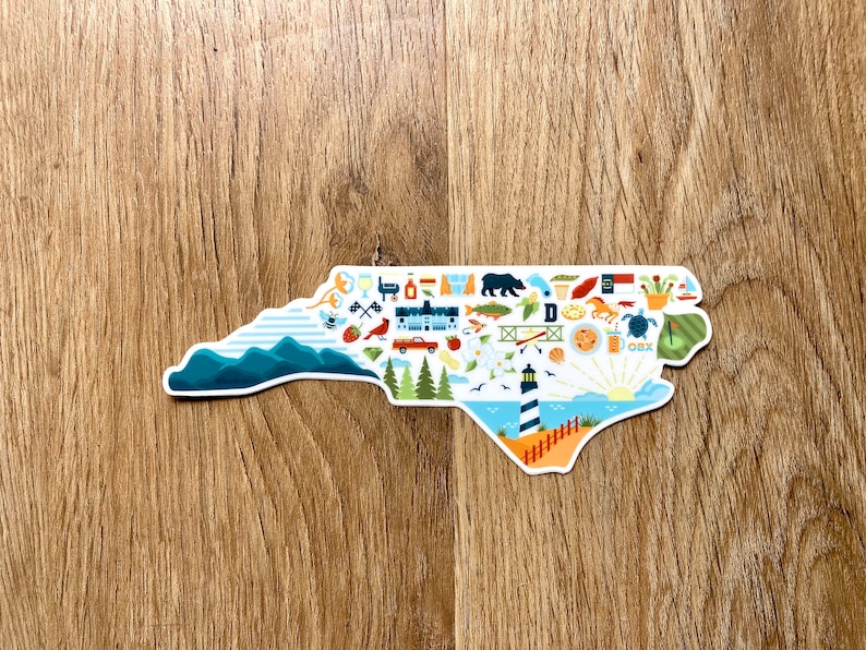 Pu&ograve; includere: Un adesivo bianco a forma dello stato della Carolina del Nord, pieno di icone colorate che rappresentano vari aspetti dello stato, tra cui montagne, spiagge, fari e cibo. Il testo "OBX" &egrave; visibile nell'angolo in basso a destra.