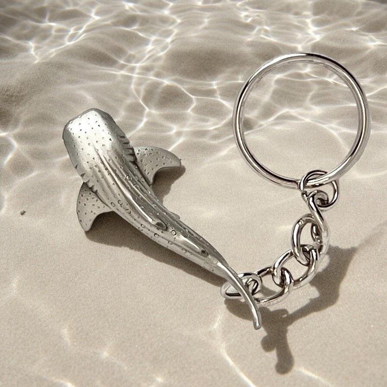 May include: A silver-colored whale shark keychain. The keychain features a detailed whale shark pendant with a textured surface and a chain connected to a metal ring. The design is aquatic-themed.