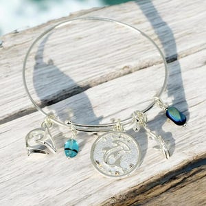 May include: Silver charm bracelet with a dolphin charm, a blue glass bead, a silver dolphin charm, and a silver charm with a dolphin and the text "I love dolphins".