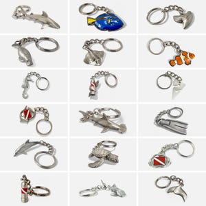 May include: A collection of silver-toned metal keychains featuring various marine life and diving-related designs. The keychains include sharks, fish, a seahorse, a stingray, a turtle, a dolphin, a scuba tank, and a diver's fin. Each keychain has a metal ring.