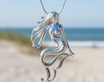 May include: A polished silver-tone pendant shaped like a mermaid with flowing hair and a detailed tail, suspended from a matching silver-tone chain. The pendant features a smooth, reflective metallic finish and an openwork design throughout the figure.