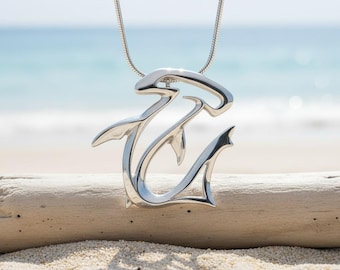 May include: A polished silver-toned pendant shaped like a hammerhead shark, suspended from a matching thin snake chain. The pendant features a stylized, open-work design that captures the distinct silhouette of the shark's head and fins.