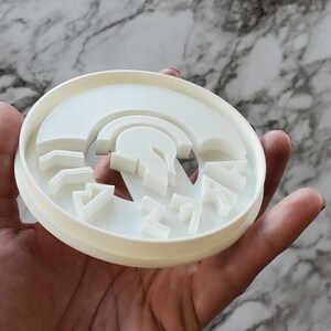 Op de afbeelding: Witte plastic koekjesvormer met een Spartaans helmdesign en het woord "SPARTAN" eromheen.