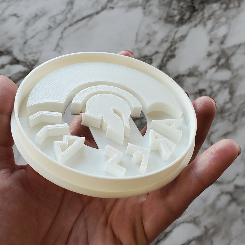 Op de afbeelding: Witte plastic koekjesvormer met een Spartaans helmdesign en het woord "SPARTAN" eromheen.