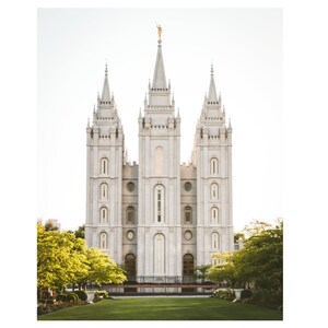 May include: A white, three-spired building with a tall, pointed roof and many windows. The building is surrounded by green grass and trees.