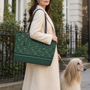 May include: A rectangular dark green tote bag featuring a repeating pattern of dog silhouettes in a lighter shade of green. The bag has two black shoulder straps, a solid green base, and gold-toned hardware accents on the strap attachments.