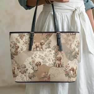 Könnte beinhalten: Beige Tragetasche mit Patchwork-Design mit Bildern von kleinen Hunden und Blumenmustern. Die Tasche hat schwarze Griffe und Verzierungen, eine rechteckige Form und ein strukturiertes Design.